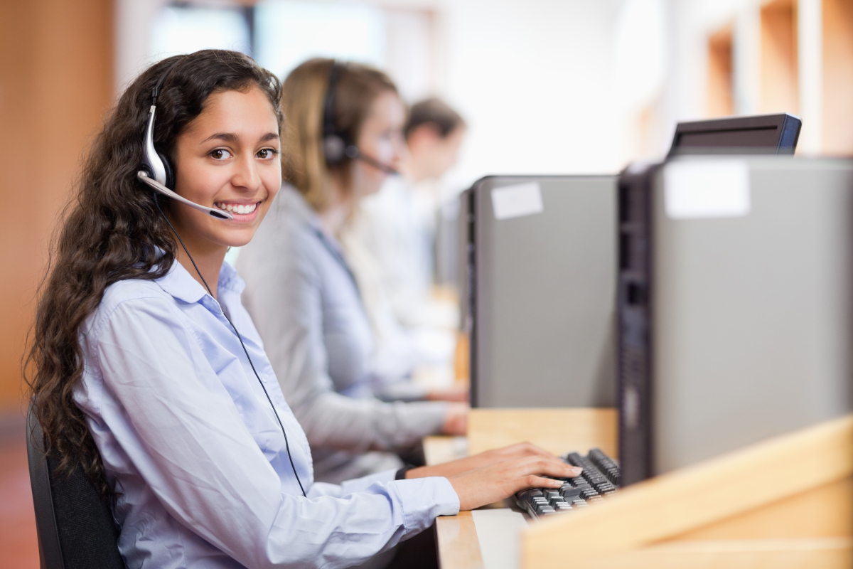 lächelnde Frau mit Headset sitzt an einem Rechner